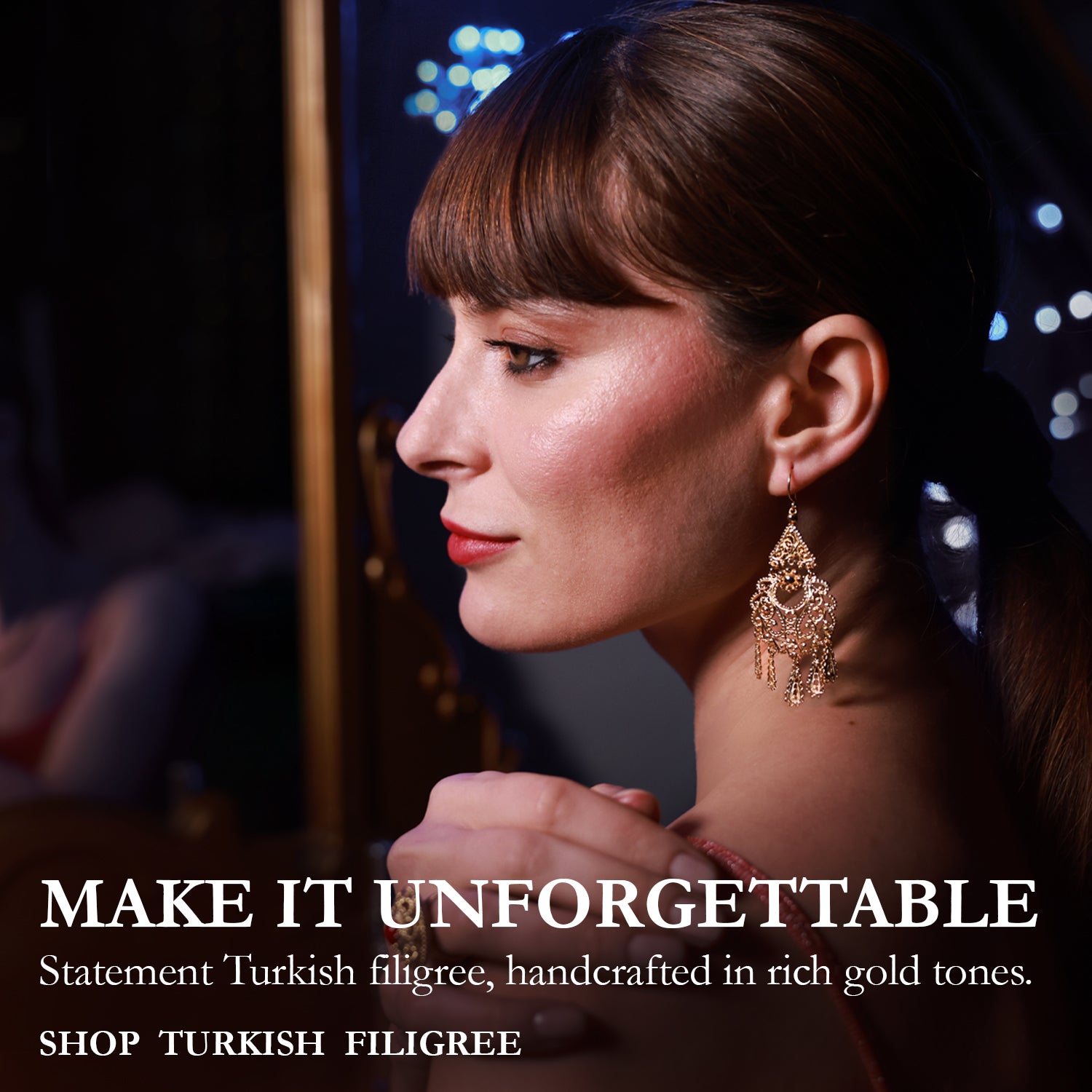 A woman in profile wearing ornate gold statement earrings and a ring, with her hands clasped in front of a mirror showing the back of the earrings. The image has a dark, elegant background with bokeh lights and text on the left reading 'MAKE IT UNFORGETTABLE' and 'Statement Turkish filigree, handcrafted in rich gold tones.