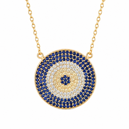 A gold-tone circular pendant necklace featuring concentric evil eye style rings of deep blue, clear, and gold pavé stones, suspended from a gold chain on a white background.