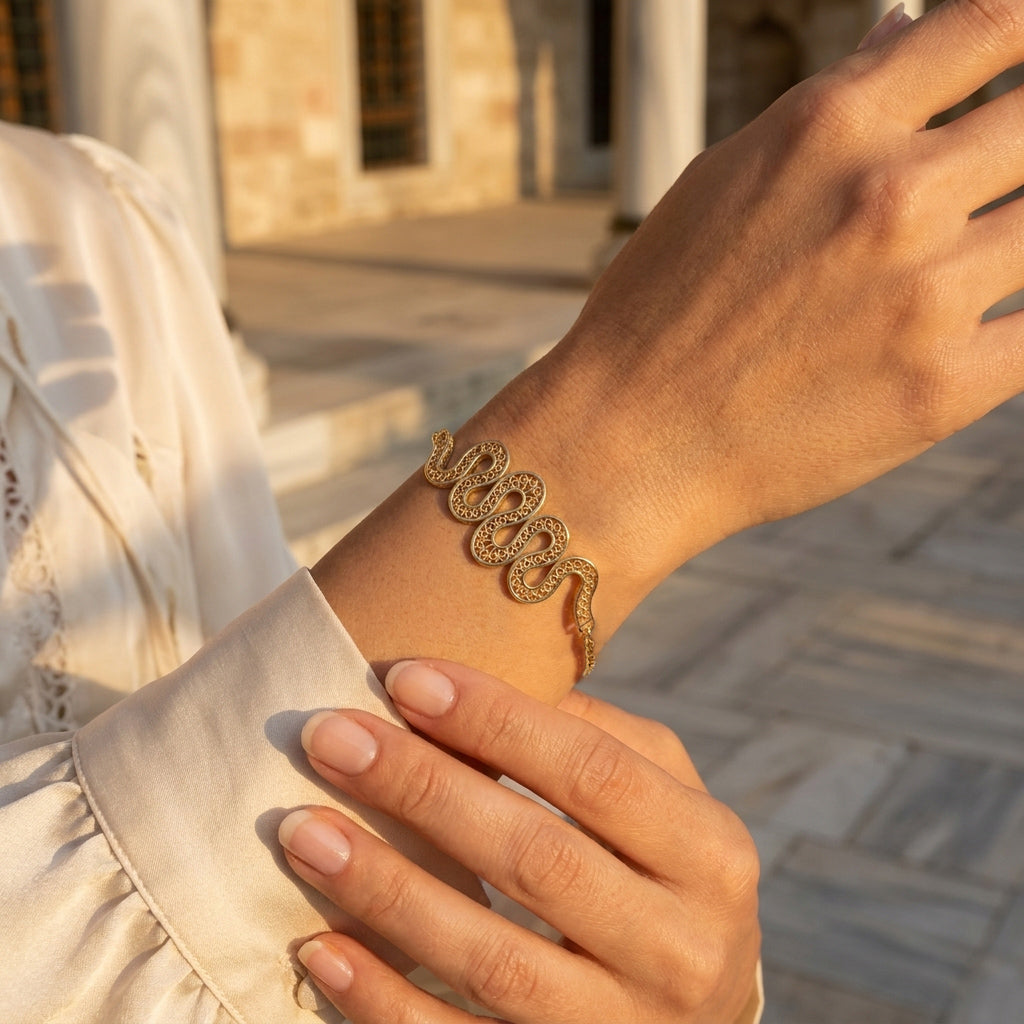 A gold snake bracelet with sparkling clear stones, worn on a woman's wrist in warm outdoor sunlight.