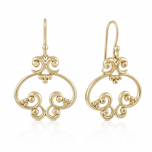 A pair of gold filigree dangle earrings with intricate scrollwork and small bead accents, shown on a clean white background with a subtle reflection.