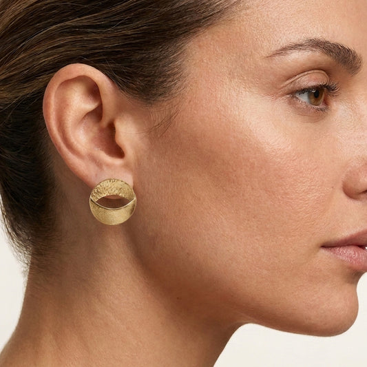 A close-up side profile of a woman wearing a textured gold hoop earring.