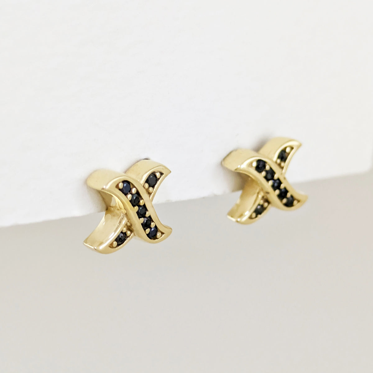 A pair of gold cross stud earrings with small black gemstone accents, shown against a clean white background.