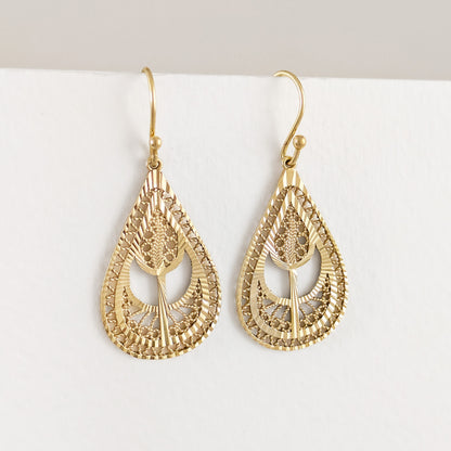 A pair of gold teardrop-shaped dangle earrings with intricate filigree cutouts and textured details, hanging against a clean white background.