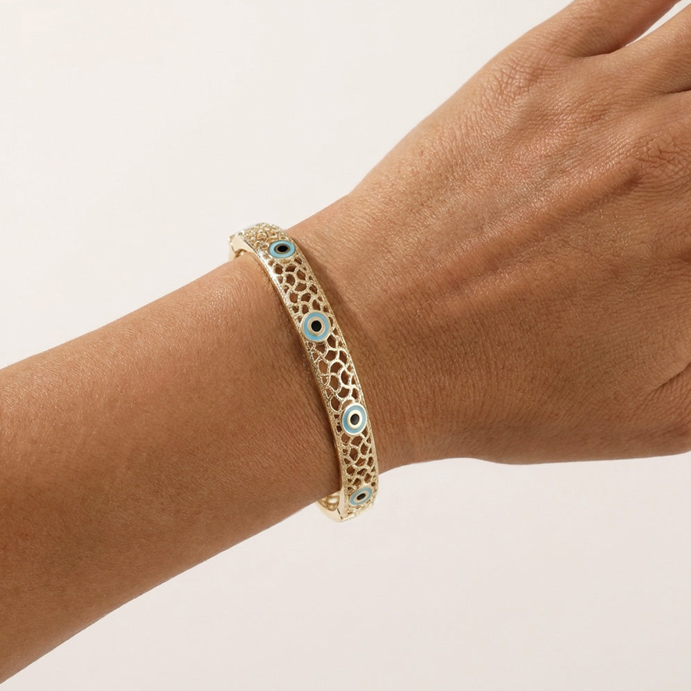 A gold-toned filigree bangle bracelet with small blue and white evil eye charms, shown worn on a person's wrist against a plain light background.