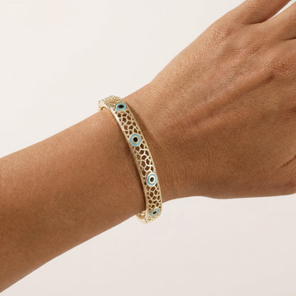 A gold-toned filigree bangle bracelet with small blue and white evil eye charms, shown worn on a person's wrist against a plain light background.