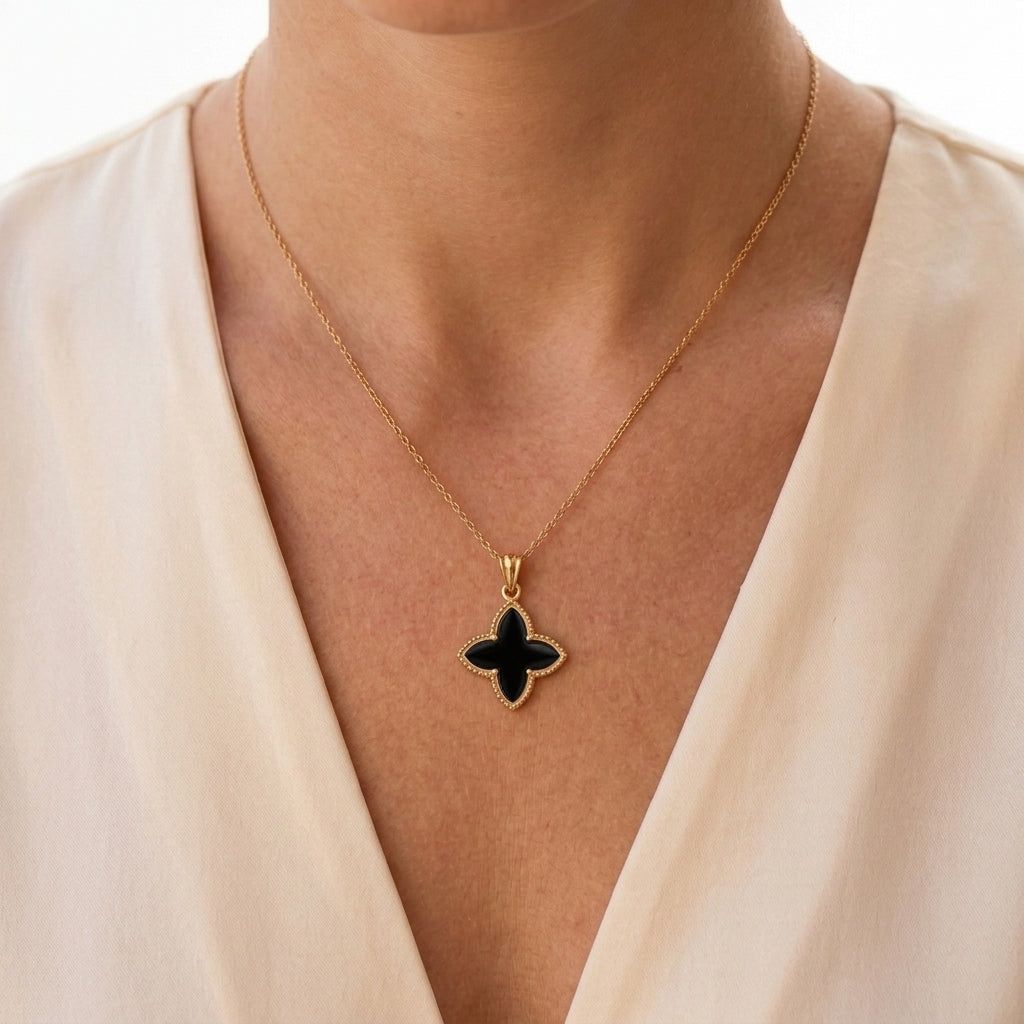 A gold chain necklace with a black enamel quatrefoil pendant, worn by a model in a cream-colored V-neck top.