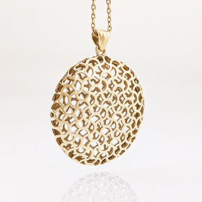 A gold pendant necklace featuring an intricate, openwork geometric mesh pattern on an oval pendant, suspended from a matching chain against a clean white background.