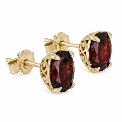 A pair of gold stud earrings featuring oval-cut dark red garnet gemstones in ornate filigree settings, shown on a clean white background.